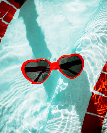 Red heart-shaped sunglasses floating in clear blue water.