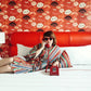 Woman lounging on Austin Motel bed wearing cotton striped serape robe and heart shaped sunglasses holding a cord phone to her ear