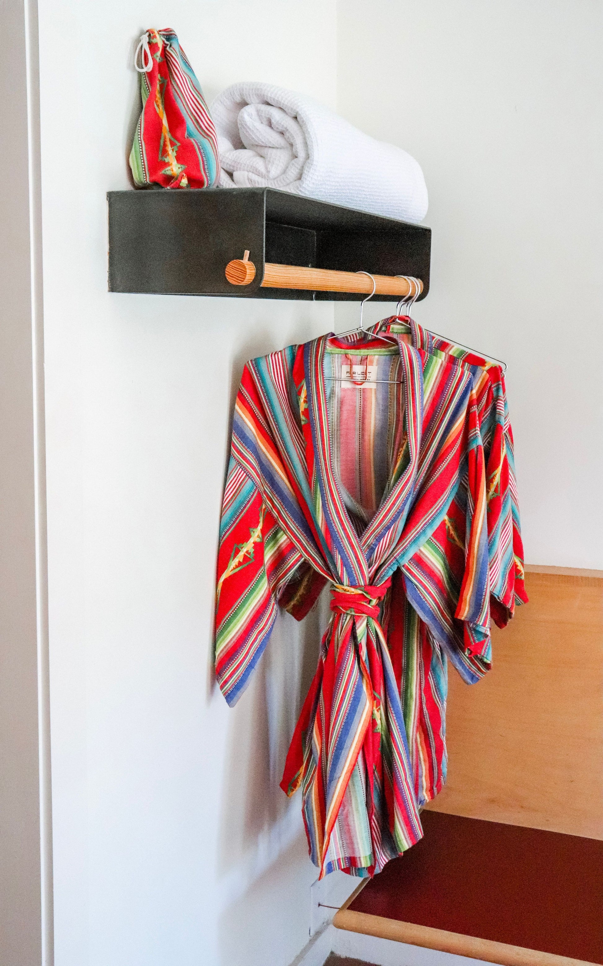 Photo of two cotton red blue yellow green striped serape robes hanging on a clothes bar inside of Austin Motel room